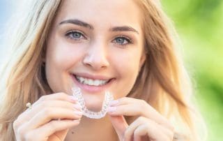 Woman posing with Invisalign aligners in hand, sporting a wide bright smile.