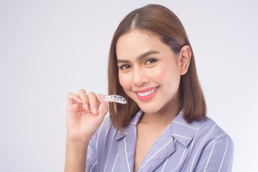 family dentist Bethesda | Happy woman holding invisalign aligners.