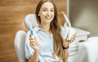 Teenage girl sitting happily, holding a model tooth in one hand and a toothbrush in the other.