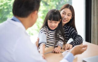 Adorable child sitting on her mother's lap, showing her hand to a gentleman dentist.