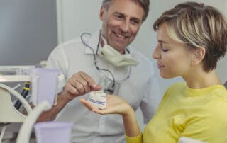 Dentist demonstrates dental bridges to the patient, placing a teeth dummy on her hand lap.