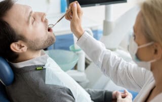 Dentist inserting dental mirror into patient's mouth for examination.