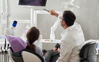Dentist displaying treatment results to patient on medical monitor.