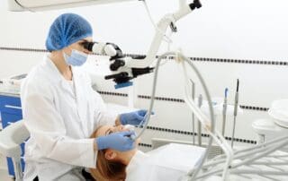 Focused dentist providing dental treatment to patient lying on medical chair, examining under microscope.