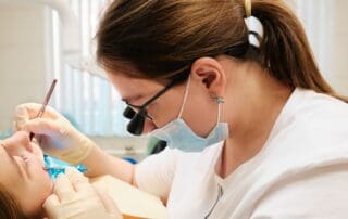 Focused dentist closely examining patient's teeth with the assistance of dental microscopic glasses.