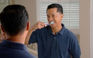 Male patient brushing his teeth and smiling while looking at himself in the mirror.