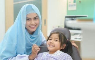 Female dentist smiling while posing with a cute little girl during dental treatment.