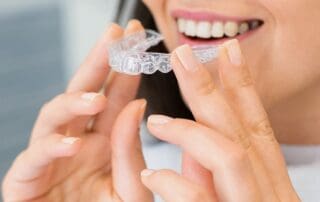 Smiling woman looking happy while applying Invisalign aligners on her teeth.