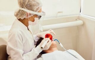 Dentist in surgical uniform, mask, and gloves providing dental treatment to the patient, handling medical instruments.