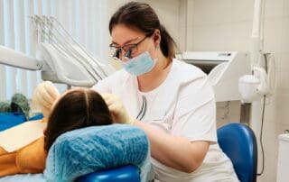 Dentist wearing dental lope glasses observes patient's mouth during examination.