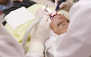 Dentist performing dental treatment on a patient with instruments in their mouth.