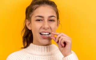 Teen girl applying Invisalign aligners to her teeth.